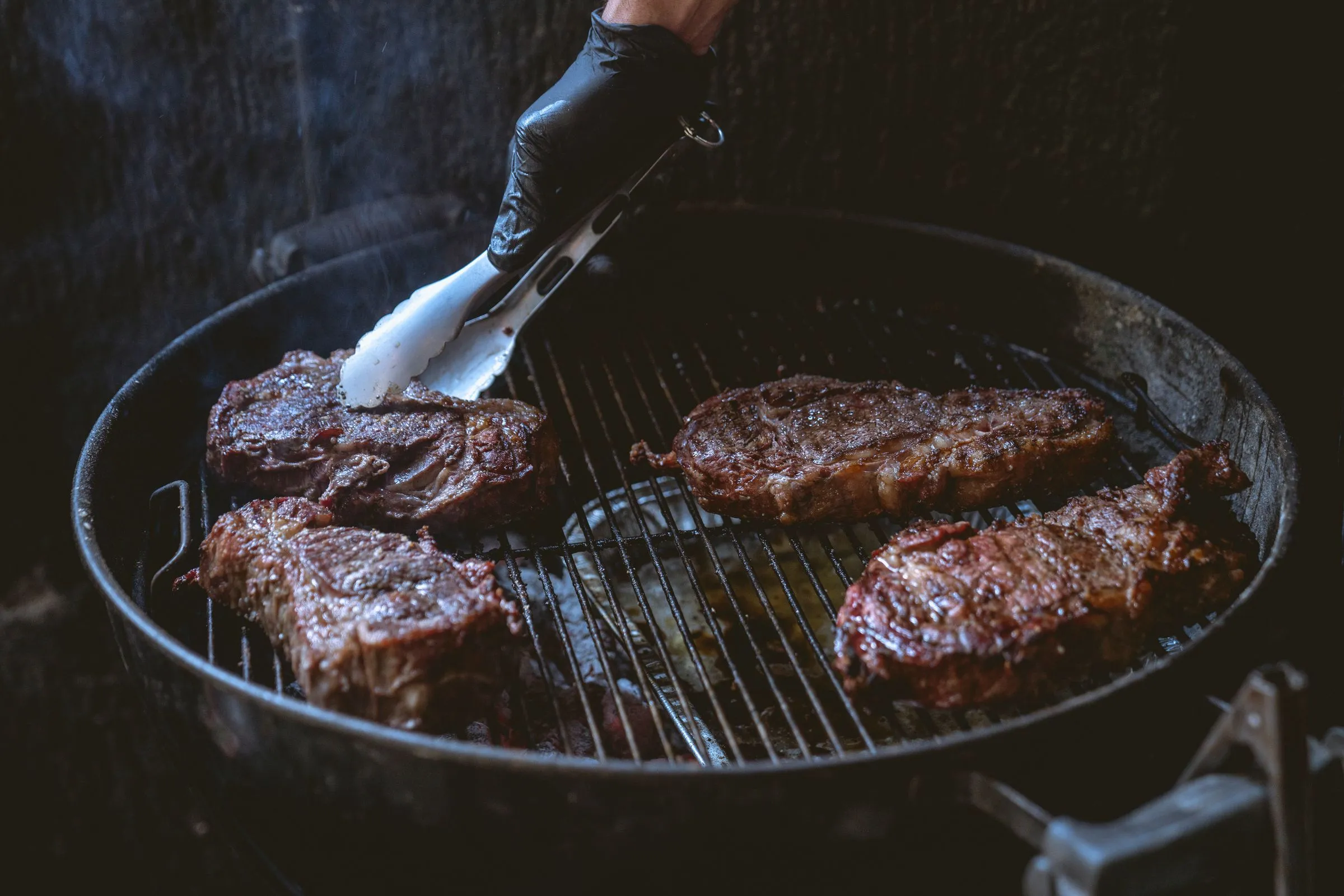 Piezas de vaca a la brasa recién volteadas con unas tenazas sobre carbón